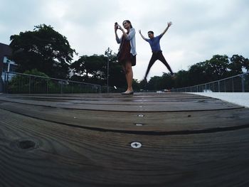 Full length of young woman jumping against trees against sky