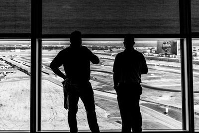 Rear view of silhouette man standing by window