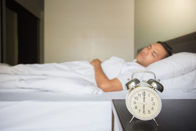 Man sleeping on bed by alarm clock at night table in bedroom