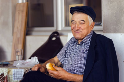 Portrait of smiling man eating bread while sitting at home