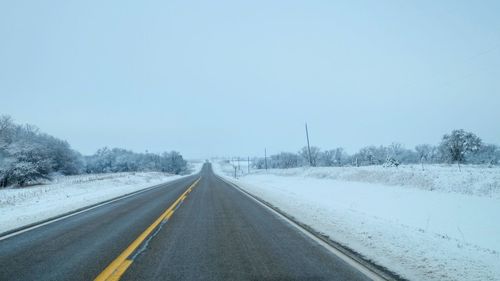 View of road amidst snow covered field against sky