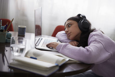 Girl doing homework with laptop at dining table