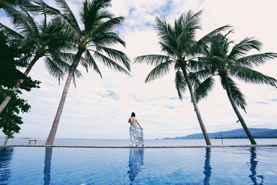 Rear view of woman standing by palm trees