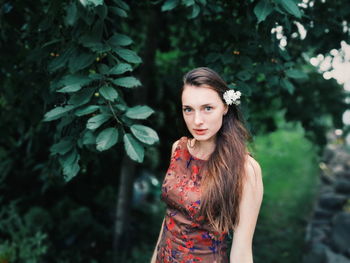 Portrait of young woman standing against tree