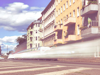 Cars on road by buildings against sky in city