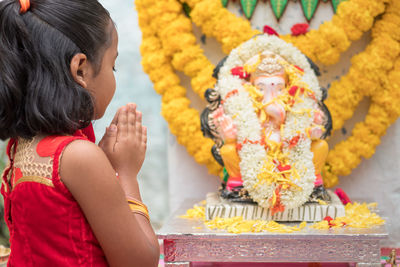 Cute girl praying with folded hands while standing by statue of lord ganesha during ganesh chaturthi festival