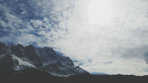 Scenic view of rocky mountains against cloudy sky on sunny day