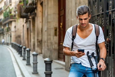 Young latin man with crutches and mobile in the street