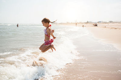 Side view of girl playing in sea against sky