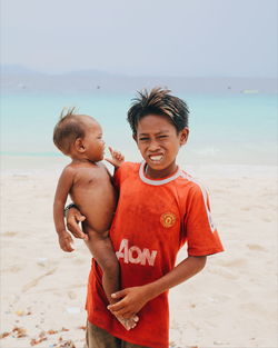 Portrait of boy carrying brother while standing at beach