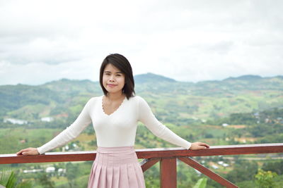 Portrait of woman standing by railing against landscape