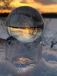 Close-up of snow covered glass on field against sky during sunset