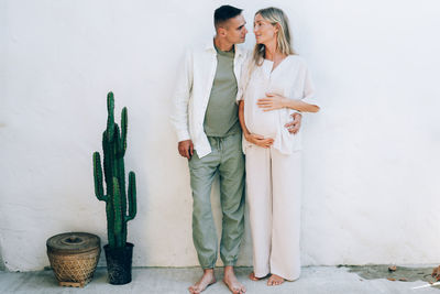 A married pregnant couple stands against a white wall. tender love relationship of a man and a woman