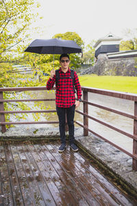 Portrait of man with umbrella standing on bridge during rainy season