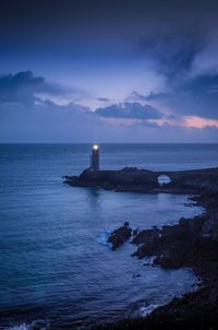 Lighthouse by sea against sky during sunset