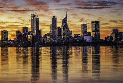 Sea by buildings against sky during sunset