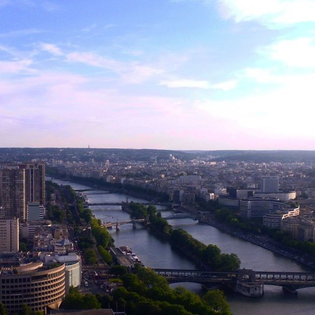 architecture, cityscape, built structure, building exterior, city, high angle view, crowded, sky, river, residential district, water, residential building, cloud - sky, tree, city life, residential structure, bridge - man made structure, aerial view, connection, cloud