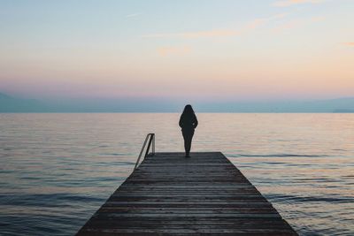 Woman standing on pier over sea against sky during sunset