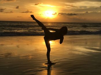 Silhouette woman exercising at beach against sky during sunset