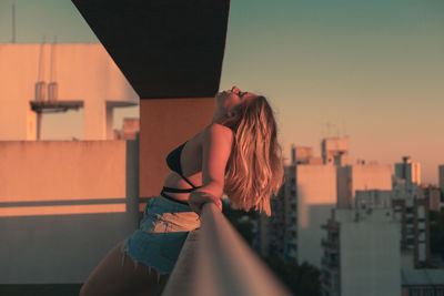 Side view of woman standing by railing during sunset