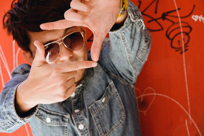 Portrait of man making finger frame while standing against wall