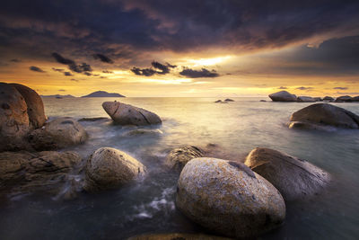 Rocks on sea shore against sky during sunset