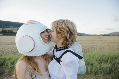 Smiling mother wearing space helmet embracing son at field