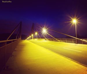 Illuminated road by bridge against sky at night