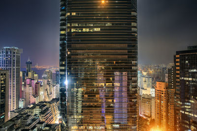 Illuminated modern buildings in city against sky at night