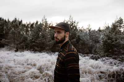 Side view of young man looking away against trees