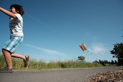 Boy flying kite on road during sunny day