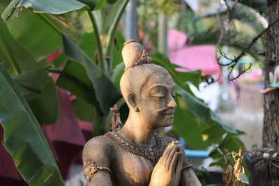 A stone man statue with green banana leaves background