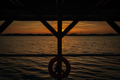 Silhouette wheel by sea against sky during sunset