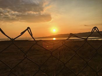 Chainlink fence against sky during sunset