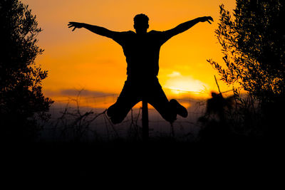 Silhouette man with arms outstretched standing against orange sky