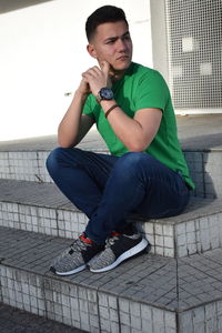 Young man looking away while sitting outdoors