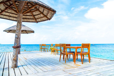 Wooden chairs and table on beach against sky