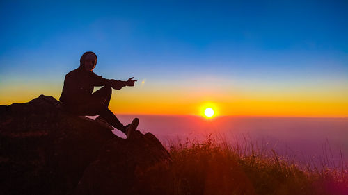 Side view of man standing on rock against clear sky during sunset