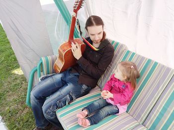 High angle view of man holding guitar while sitting with girl on sofa at field