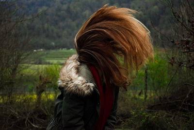 Young woman tossing hair while standing on field against trees