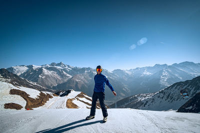 Scenic view of a person in skiing gear standing in front of snowcapped mountains against sky