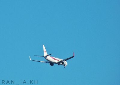 Low angle view of airplane flying against clear blue sky