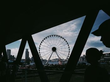 Silhouette people at amusement park against sky