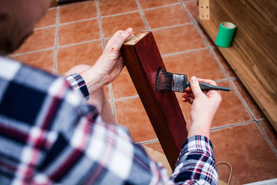 Midsection of young man painting wooden plank while sitting at home