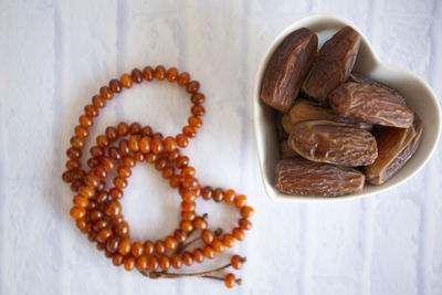 High angle view of dates in heart shape bowl by prayer beads on table