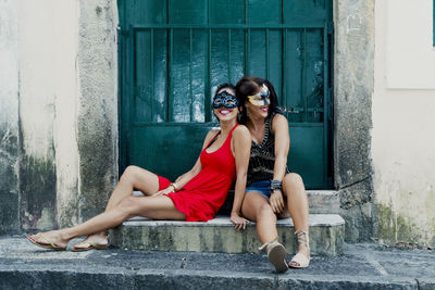 Portrait of two women wearing carnival mask sitting against old historic door.