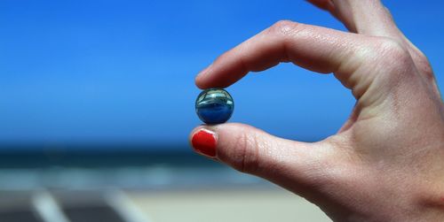 Cropped hand of woman holding marbles against blue sky