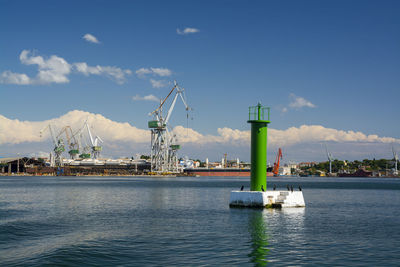 Dock cranes in sea against sky