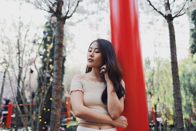 Young woman looking down while standing against plants in park