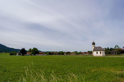 House on field by buildings against sky